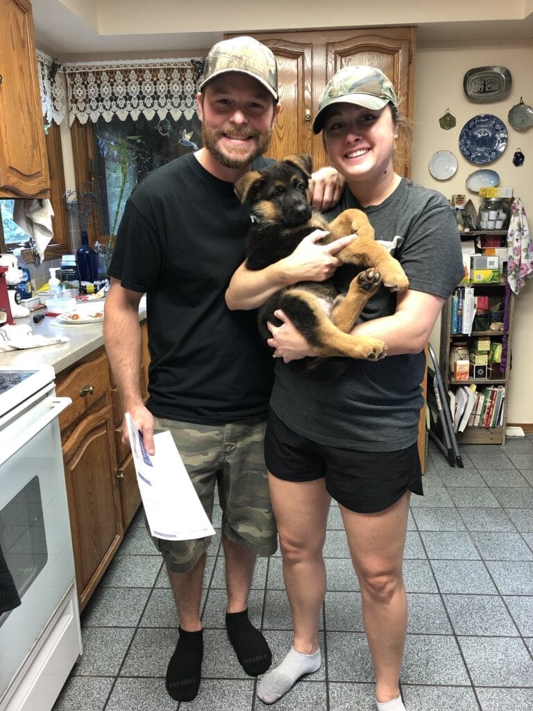 A man and woman holding a dog in their kitchen.